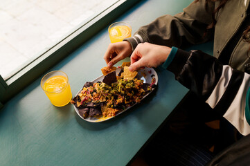 Two friends are enjoying a plate of nachos with guacamole, accompanied by glasses of refreshing orange juice, during a casual meal at a restaurant