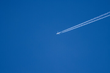Un avión surca un cielo azul claro, dejando rastros de estelas blancas. Una escena que transmite...