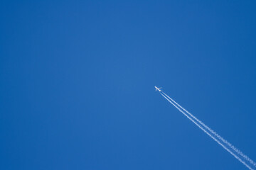 Un avión surca un cielo azul claro, dejando rastros de estelas blancas. Una escena que transmite libertad, exploración y tranquilidad en las alturas.