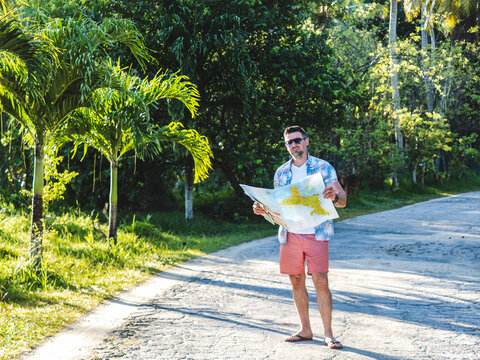 Handsome man in sunglasses looking at map with landmarks against palm trees background. Beautiful views and sights of Seychelles. Clear, sunny day. Concept of leisure and travel