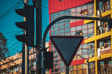 Fototapeta premium “Yield to traffic” sign. A red building with a white triangle sign on a pole. The sign is red and white and is pointing to the left.