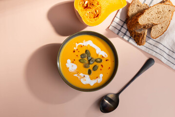 Creamy pumpkin soup served in deep bowl, topped with a swirl of cream and garnished with fresh herbs. A comforting, hearty dish perfect for autumn evenings, blending smooth textures and rich flavors.
