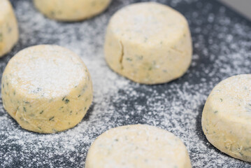 Frozen syrniki (cottage cheese pancakes) flavored with creamy cheese and dill on a dark black background, semi-finished and ready for cooking. 