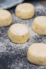 Frozen syrniki (cottage cheese pancakes) flavored with creamy cheese and dill on a dark black background, semi-finished and ready for cooking. 