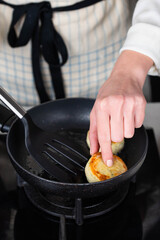 Hands of a female chef frying and baking homemade savory syrniki (cottage cheese pancakes) with creamy cheese and dill in a pan, sizzling in oil. Concept of home cooking and traditional recipes