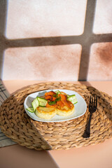 Syrniki with creamy cheese and dill, served on plate with fresh cucumber slices, thinly sliced smoked salmon, and herbs. Concept of traditional home recipes, and balanced meals.