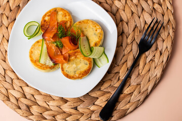 Syrniki with creamy cheese and dill, served on plate with fresh cucumber slices, thinly sliced smoked salmon, and herbs. Concept of traditional home recipes, and balanced meals.