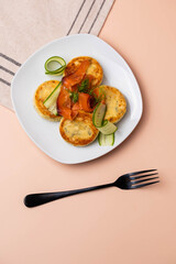 Syrniki with creamy cheese and dill, served on plate with fresh cucumber slices, thinly sliced smoked salmon, and herbs. Concept of traditional home recipes, and balanced meals.