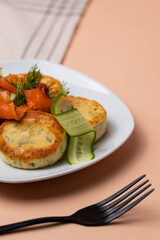 Syrniki with creamy cheese and dill, served on plate with fresh cucumber slices, thinly sliced smoked salmon, and herbs. Concept of traditional home recipes, and balanced meals.