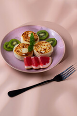 Sweet classic breakfast syrniki (cottage cheese pancakes) served on a plate, with vibrant slices of grapefruit, fresh kiwi, and mint. Home cooking, traditional recipes, and delicious morning meals.