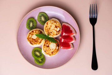 Sweet classic breakfast syrniki (cottage cheese pancakes) served on a plate, with vibrant slices of grapefruit, fresh kiwi, and mint. Home cooking, traditional recipes, and delicious morning meals.
