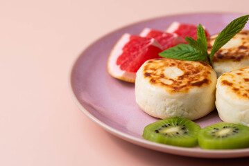 Sweet classic breakfast syrniki (cottage cheese pancakes) served on a plate, with vibrant slices of grapefruit, fresh kiwi, and mint. Home cooking, traditional recipes, and delicious morning meals.