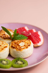 Sweet classic breakfast syrniki (cottage cheese pancakes) served on a plate, with vibrant slices of grapefruit, fresh kiwi, and mint. Home cooking, traditional recipes, and delicious morning meals.