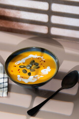 Creamy pumpkin soup served in deep bowl, topped with a swirl of cream and garnished with fresh herbs. A comforting, hearty dish perfect for autumn evenings, blending smooth textures and rich flavors.