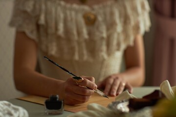 Close up of classic young lady writing letter with focus on female hands holding intricate ink pen and ornate ring, copy space
