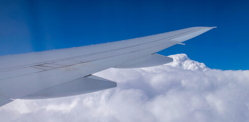 Wing of airplane flying above the clouds in the blue sky background.