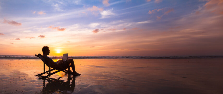 freelance work, financial freedom, silhouette of  business man working on laptop on sunset beach, banner background with copyspace