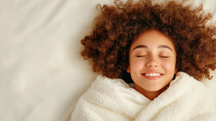 A young girl with curly hair wrapped in a cozy white blanket smiles peacefully, eyes closed in blissful contentment.