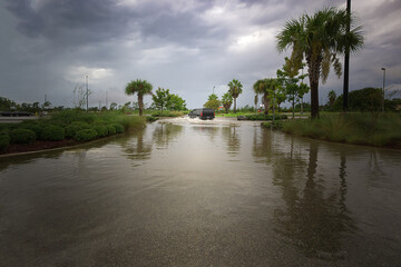 vehicle driving in parking lot submerged under heavy rain, with water pooling  creating  stormy scene.