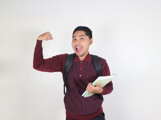 Young winner smart asian boy student he wear maroon t-shirt casual clothes backpack bag hold books showing hand biceps muscles. High school university college concept