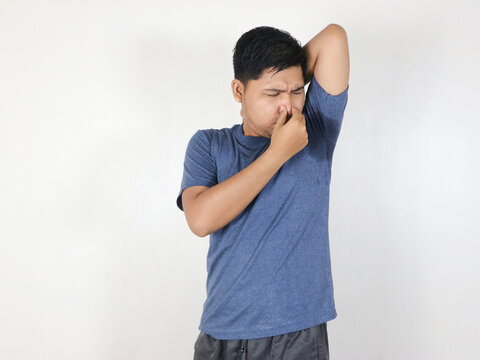 Asian man is checking his odor underarm, close his nose with hand, feel disgusted the body strong smell. Concept , health problem. Unpleasant body odor , smell nasty reaction. Negative emotion.