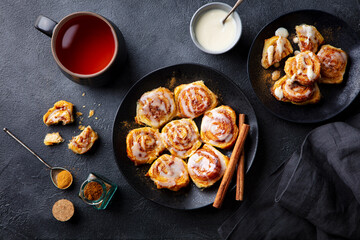 Cinnamon rolls, buns, cinnabons on black plate with cup of tea. Dark background. Top view.