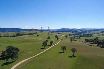 Obraz premium Aerial view of a rural landscape with rolling green fields wind turbines and a clear blue sky creating a peaceful scene 