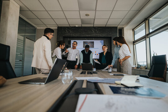 A multicultural group of business people engaging in a strategy meeting in a modern office setting, focusing on presentation and collaboration. Laptops and documents are scattered across the table.