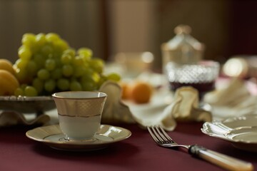Close up of single tea cup and saucer with blurred fruit and cutlery in background on crimson...