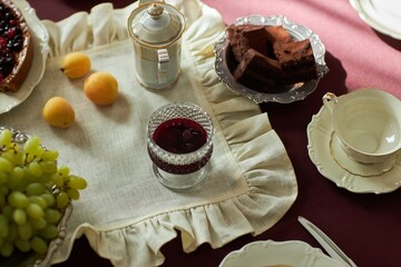 Top view of vintage table set with elegant tea service, fresh fruit and desserts on red velvet background, copy space