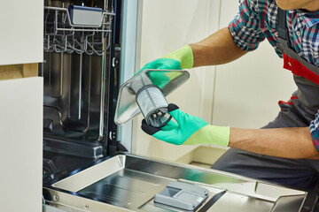 An Appliance Repair Technician is servicing a dishwasher in a modern kitchen. A skilled technician...
