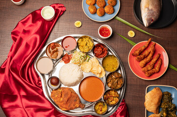Goan fish thali with prawns, soul curry, rice, sweet dish, gulab jamun on red and brown background...