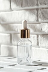 Clear glass dropper bottle with golden cap placed on white brick wall and wooden table