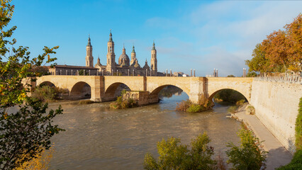 Obraz premium Puente de Piedra Framed by Trees and Basilica del Pilar in Zaragoza