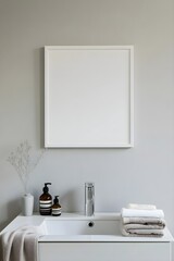 A blank white frame hanging above a sink, captured from the entrance, with folded towels and toiletries in view.