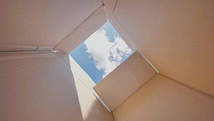 Open cardboard box is revealing a blue sky with some clouds, suggesting freedom, hope and new...