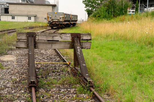 Old weathered wooden and steel buffer stop at the end of a railroad track. In the background two transortation wagons are standing on the railroad track.