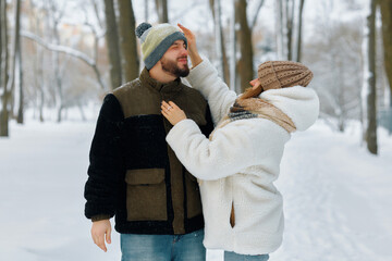 A couple smiles and engages in a playful moment during a winter stroll in a snowy park, with...