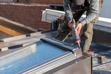 Construction worker using silicone sealant adhesive to fix a metal sheet on the skylight window. A roofer and window master work.