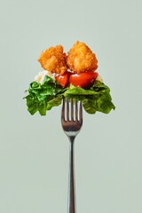 Crispy chicken salad fork with lettuce, tomato, and cheese on minimalist background