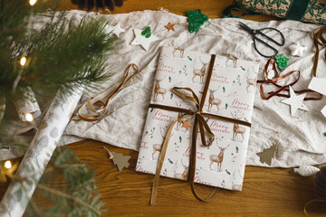 Merry Christmas! Stylish christmas gift flat lay, modern paper ornaments and pine branches on rustic table with golden christmas lights. Atmospheric christmas eve. Modern wrapped present