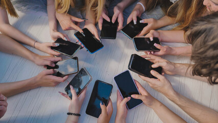 People holding their smartphones around a white table, using their devices and showing a sense of...