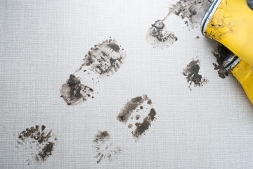 Yellow rubber boots create distinct muddy footprints on a light-colored textured surface,...