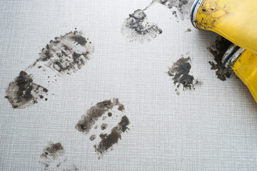 Yellow rubber boots create distinct muddy footprints on a light-colored textured surface,...