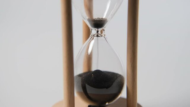 Close-up of sand flowing through a transparent hourglass, representing the relentless passage of time and approaching deadlines