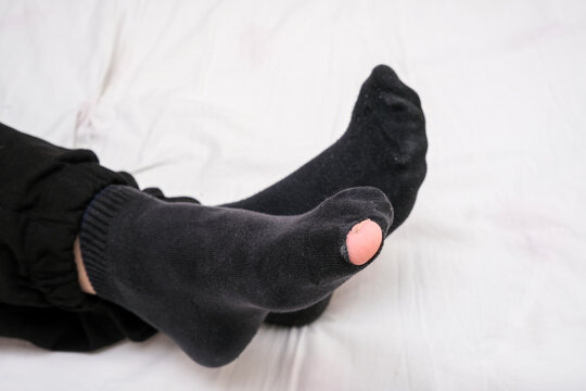 Caucasian male toe sticking out of worn out short nylon black plain socks with hole top view