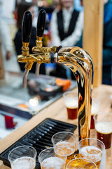 A beer tap steadily pours a frothy, delicious beer into glasses that sit ready on the table,...