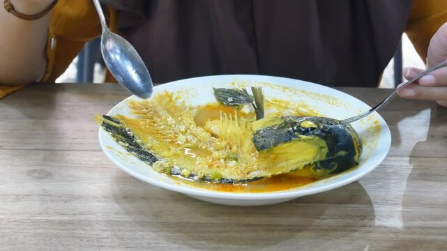 woman eats tilapia fish head curry, an Indonesian recipe with fresh sauce. close up view
