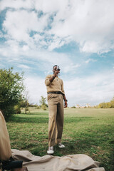 A stylish man stands in a green field, savoring a glass of wine beneath a bright, cloudy sky. The leisure setting exudes a serene and relaxed atmosphere.