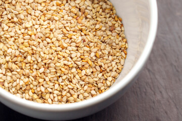 White ceramic bowl filled with raw organic sesame seeds placed on a dark wooden surface. Top view